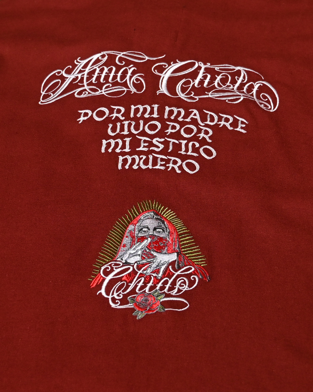 Detalle del bordado Amá Chola en camisa boxy de lino rojo tinto edición especial