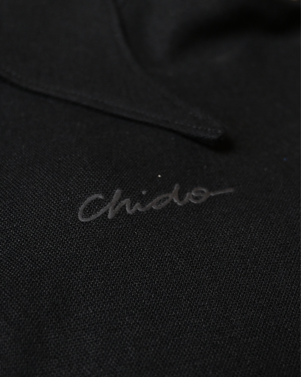 Detalle de la firma CHIDO sobre camisa de lino negra