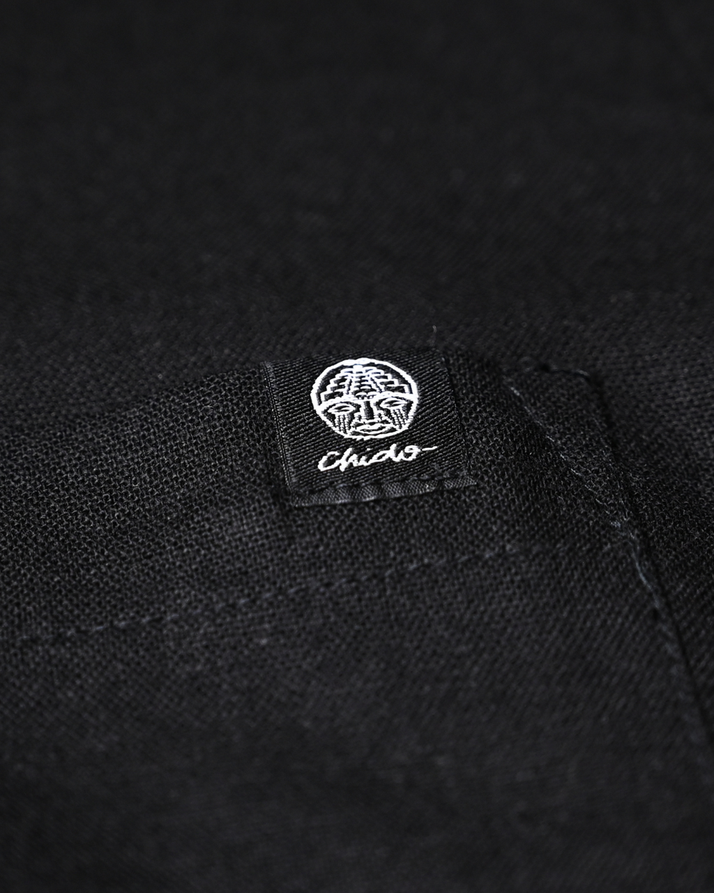 Detalle del logo bordado en camisa de lino negra CHIDO Signature.