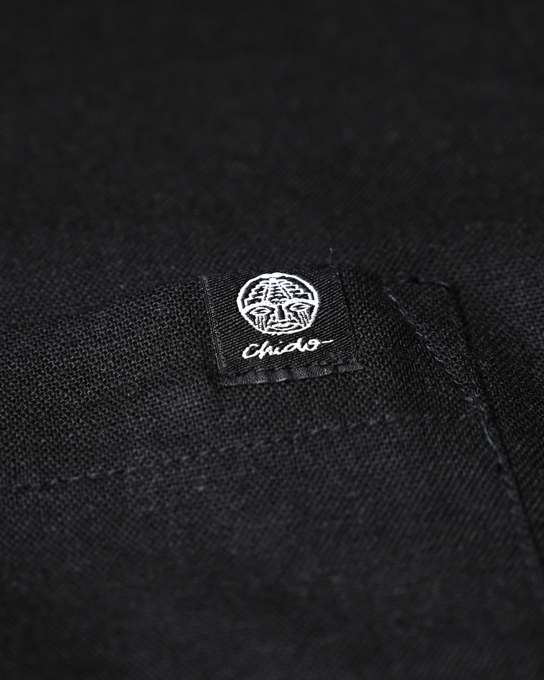 Detalle del logo bordado en camisa de lino negra CHIDO Signature.
